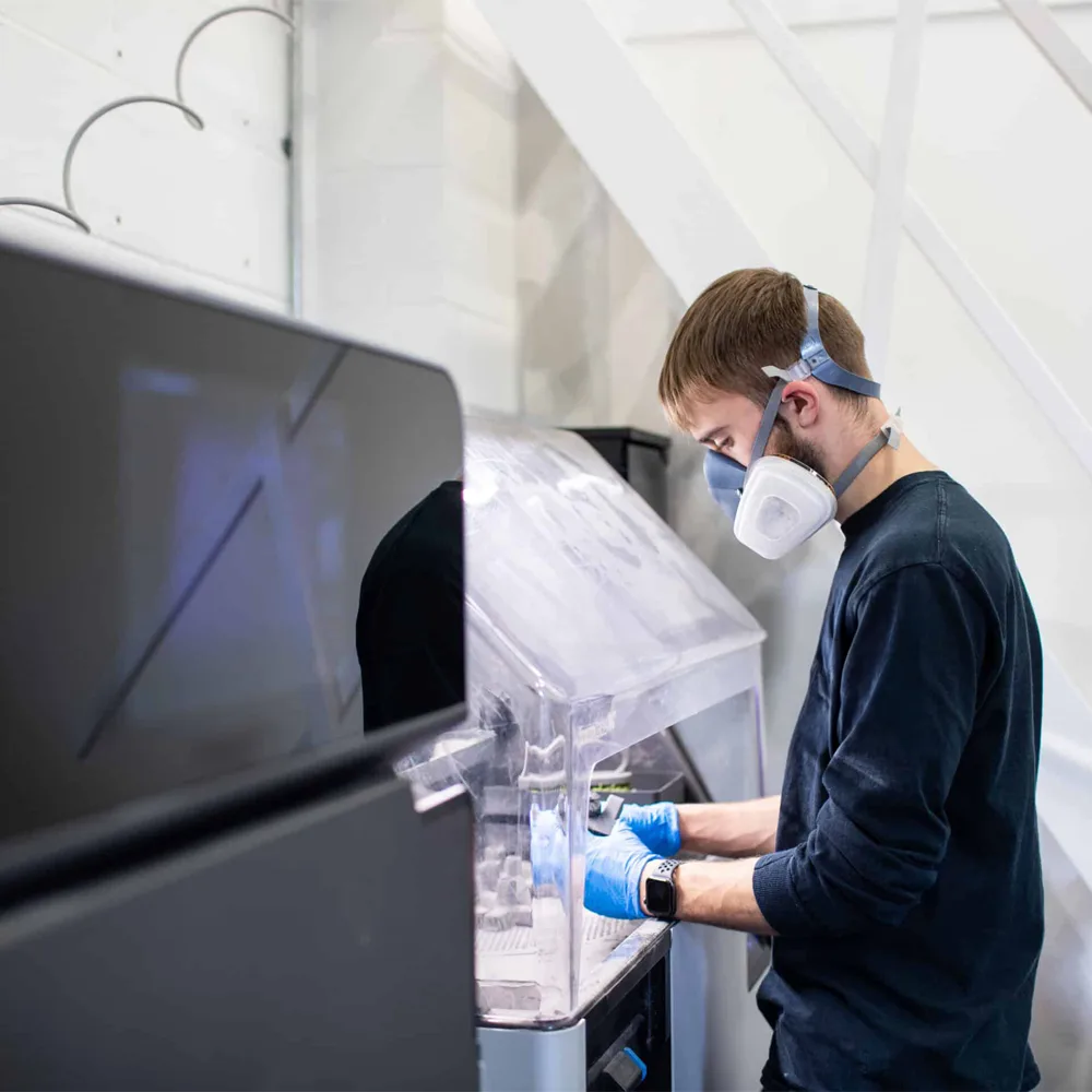 Selective Laser Sintering (SLS) 3D printed parts undergoing post-processing steps such as depowdering and surface finishing in an industrial setting