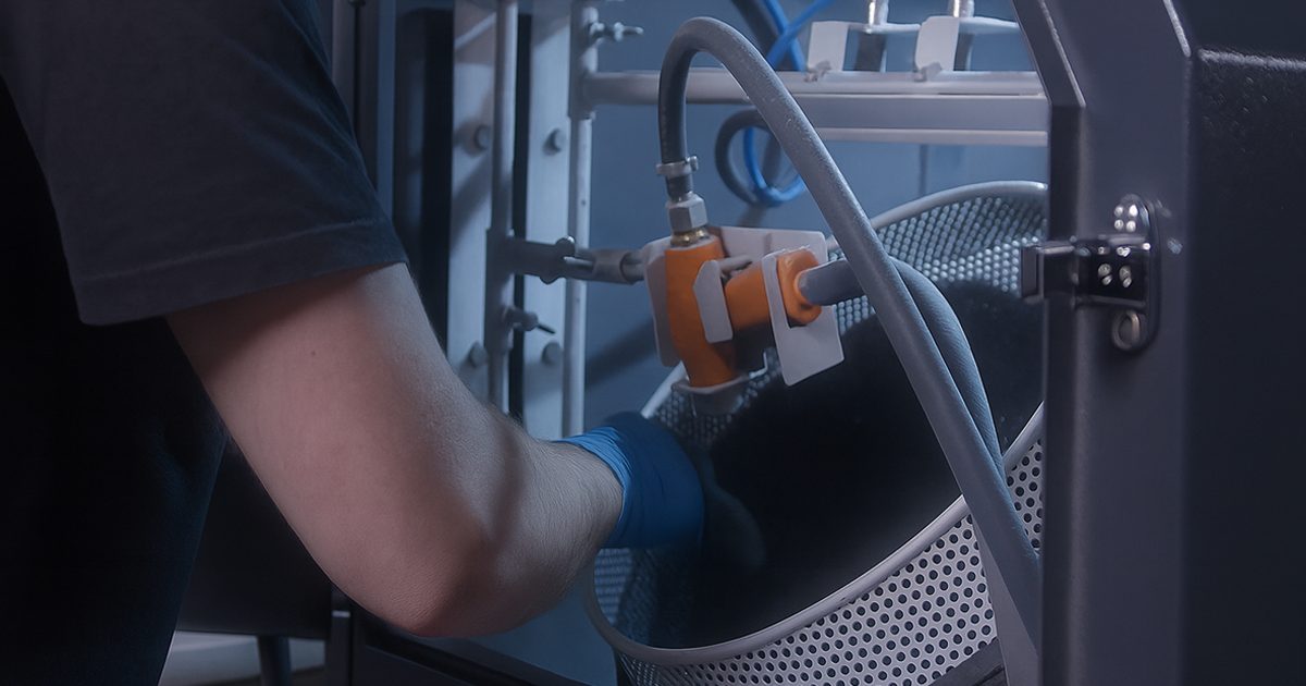 An operator unloading finished parts from an automated blasting machine, with the chamber open and freshly processed components visible inside.